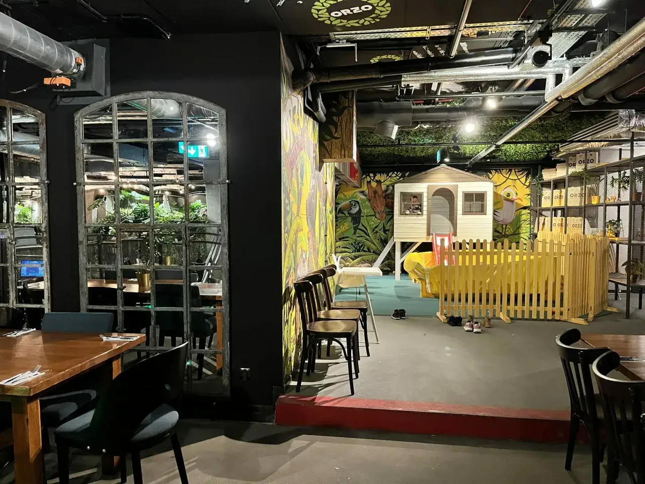 Warszawska restauracja z placem zabaw dla dzieci. Wnętrze z kolorowymi muralami, domkiem do zabawy i drewnianym płotkiem.